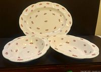 Photo showing one large 18-inch platter and two 10-inch oval open bowls, all with pink rosebud pattern and scalloped edges placed on a dark surface