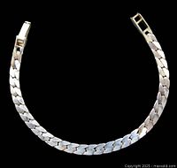 Front side of vintage men's sterling silver curb link bracelet laid open on black background showing polished flat linked chain and clasp.