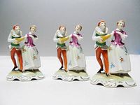 Front view of three porcelain troubadour place card holders showing detailed hand-painted figures and floral patterns.