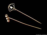 Pair of two vintage stick pins, one with single seed pearl in white and yellow gold fan-shaped setting, the other with three seed pearls in yellow gold rectangular setting, shown against black background.