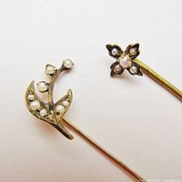 Close-up image showing the detailed floral and cross motifs on two 9k gold stick pins adorned with seed pearls. Visible light surface darkening and missing end caps.