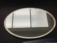 Front view of vintage oval boudoir mirror showing decorative notched edge and reflective surface.