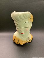 Front view showing gold flower in hair, closed eyes with detailed eyelashes, red lips, and gold highlighted collar.