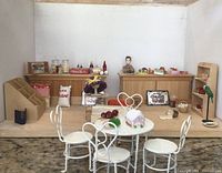 Front view of the opened dollhouse showing interior with counters, miniature cakes, and furniture.