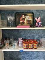 Shelf displaying a variety of advertising glassware and collectibles including Santa Claus tray, pink bunny toy, and multiple branded glasses