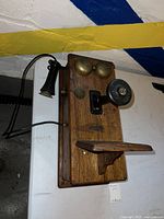 Front angle view of antique wooden telephone featuring brass bells, rotary dial, and handset hanging on the left side.