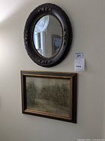 Framed original art under oval mirror on wall showing condition and size.