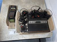 Overview of Atari 2600 console with multiple joystick controllers and 13 game cartridges in two containers.