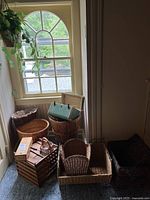 Photo showing various items including vintage suitcase, collapsible wooden crate, wooden candle box, hanging basket with faux greenery, and multiple wicker baskets grouped near a window.