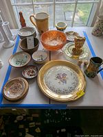 Overview of all ceramic and glass items on the table including bowls, pitchers, planters, ashtray, salt and pepper shakers, decorative plates and vases.