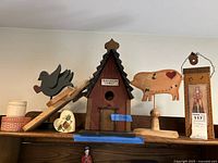Full view of eight wooden folk art items including birdhouse, animal cutouts, and stamp, arranged on shelf.