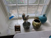 Overall view of all lot items placed on white surface by window: glass dome, ceramic bird planter, green vase, blue lidded container, porcelain butterfly frame.