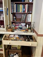 Wide shot of shelving unit with stacked books, cookbooks, baskets, and supplies on shelves and counters including stationery items and craft materials.