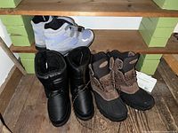 Three pairs of boots, showing two pairs clearly with one pair black insulated women's winter boots and one pair brown/black LL Bean duck boots.