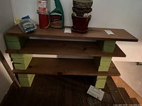 Overall view of shelving unit with three wooden boards held by stacks of green bricks