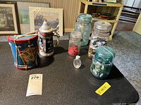 Photo showing five glass jars filled with various color buttons, a decorative ceramic drum, and a German beer stein.
