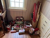 Photo showing an assortment of Christmas gift wrap items including ribbons, bows, gift bags, and various rolls of wrapping paper in a corner near a window.