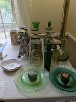 Green colored glass set including glasses, candlesticks, pitchers, and vases arranged on table near window