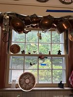 Copper kettles hanging above a kitchen window with a decorative copper plate also visible below.
