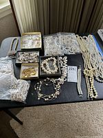 Full lot arranged on table showing multiple pearl-like necklaces, bracelets, and a few small boxes of costume jewelry items.