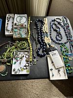 Full layout of assorted beaded and metal costume jewelry including necklaces and earrings spread on a dark surface.