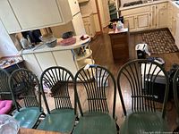 Six green wooden dining chairs aligned in a row viewed from above showing backs and seats, placed in a kitchen environment.