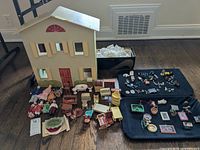 Full view of wooden dollhouse with dolls and miniature furniture arranged in front on floor.