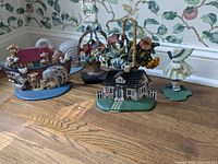 Photo showing six cast iron door stops with various designs including a girl figure, house, floral basket, and animal-themed stops arranged on a wooden floor.