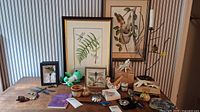 Photo of table with various bird-themed decorations, framed prints, pottery, and plush toy
