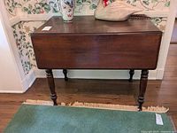 Front view of wooden drop leaf table with turned legs and drawer under table top.