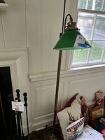 Full view of the vintage floor lamp showing the green glass shade and metal base near a fireplace and window.
