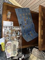 Coins and paper currency in a plastic container, with some coins arranged on blue paper by country.