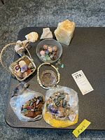 Top view of the collection on a black surface showing bags of mixed stones, a metal basket with polished stones, round polished spheres in a glass bowl, and a pale yellowish stone.