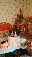 Wide shot of table featuring various Halloween and autumn decor items including pumpkins, wreaths, small figurines, and decorated pillows