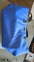 Full view of blue vinyl tote bag with black handles lying flat