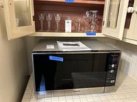 Front view of Panasonic microwave with black door and control panel on the right side with stainless steel handle, placed on kitchen counter below cabinetry.