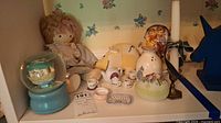Shelf with cloth doll, music boxes, Disney tea set and various ceramic decorative items including snow globe and candle holder