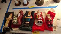 Wide view of all five Santa figurines arranged in a row on a white surface, each on a colored fabric bag.