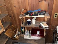 Photo of wooden tea box open showing paintbrushes inside, additional paintbrushes in front, two mugs, a box, books on shelves and a coiled dog leash on top of the shelf.