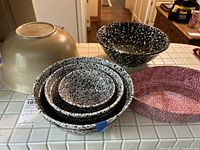 Six mixing bowls on tiled countertop: Four nested black and white Pfaltzgraff bowls, one large black speckled Springware bowl, one red elongated bowls.