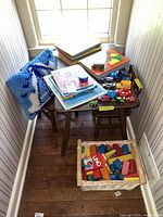 Photo showing the collection of vintage puzzles on a small wooden stool, assorted toy cars placed on the stools, a decorative blue and white pillow, and a wicker basket filled with colorful wooden blocks.