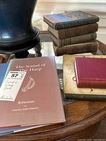 The photo shows a collection of seven vintage books stacked on a table next to a blue vase. One book titled The Sound of The Harp is laid flat and signed. Other books are stacked and have worn hardcovers in varying brown and greenish tones.