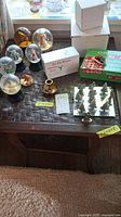 Full lot overview showing assorted snowglobes including different sizes and designs, bingo and trivia games, tic tac toe with Christmas tree pieces and brass candle holder on a wooden table.