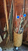 Wicker basket holding an assortment of garden stakes and markers including metal rods and circular reflectors in blue and red, leaning against a wooden wall