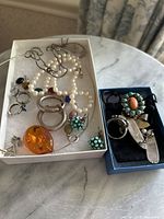 Top view of sterling silver jewelry including pearl necklaces, large hoop earrings, turquoise and amber accented pieces, and silver rings and pins.