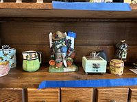 Shelf holding 7 small items including trinket boxes, pitcher, garden figurine, birdhouse box, small wooden box with clasp
