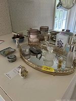 Mirrored tray with assorted perfume bottles, ceramic jars, and vanity items displayed on a white surface.