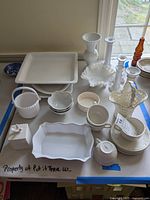 Overview of white ceramic serving platters, vases, cups and saucers, and candlestick holders along with glass bottle decor