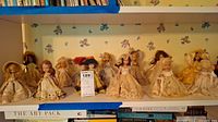 Front view showing 10 vintage dolls lined up on shelf with variety of dress styles and colors.