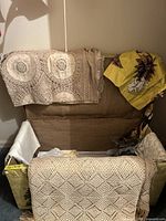 Box with assorted vintage lace and embroidered linens, including yellow floral fabric and crocheted lace pieces.